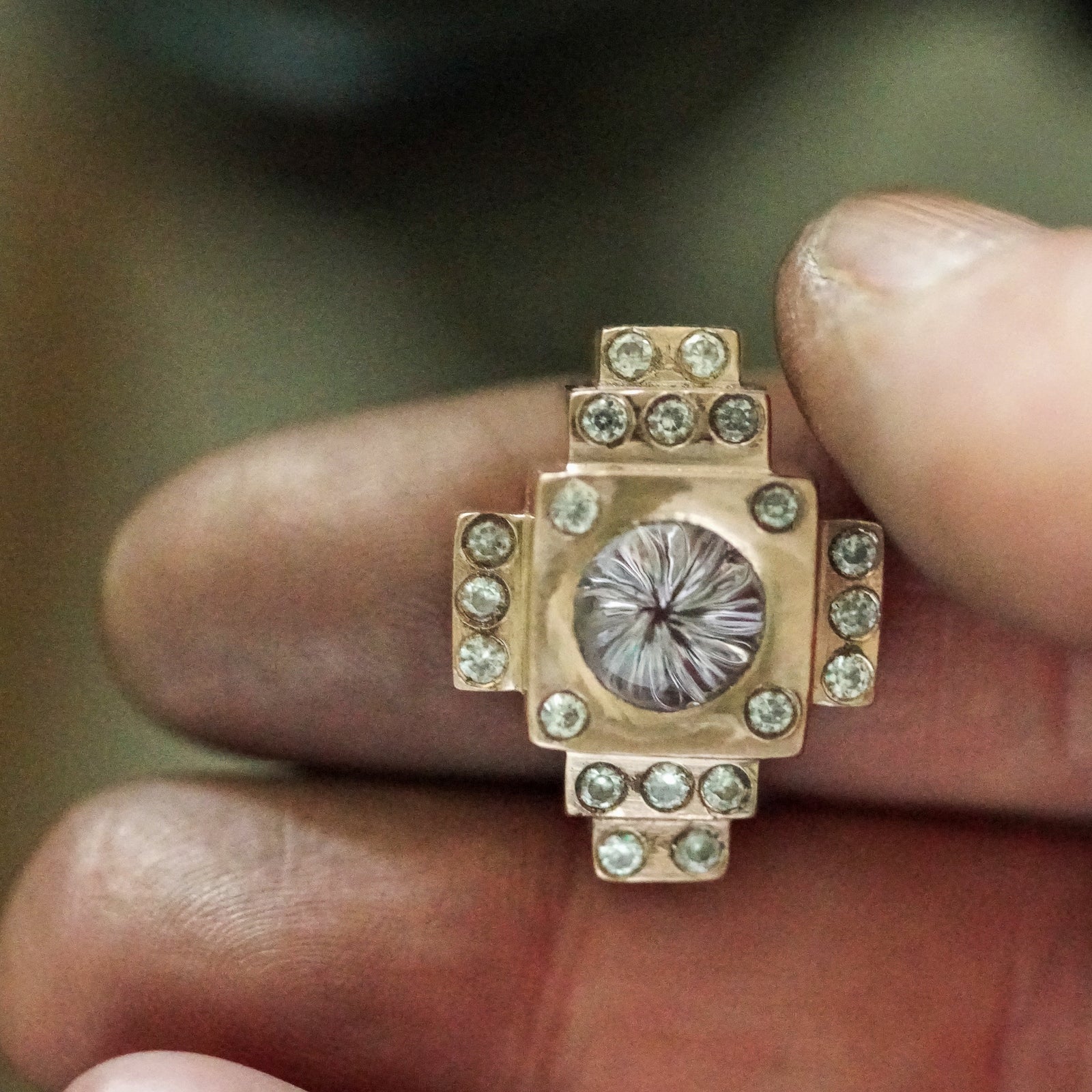 diamond engagement ring with many diamonds and vortex cut in a jeweler's dirty hand