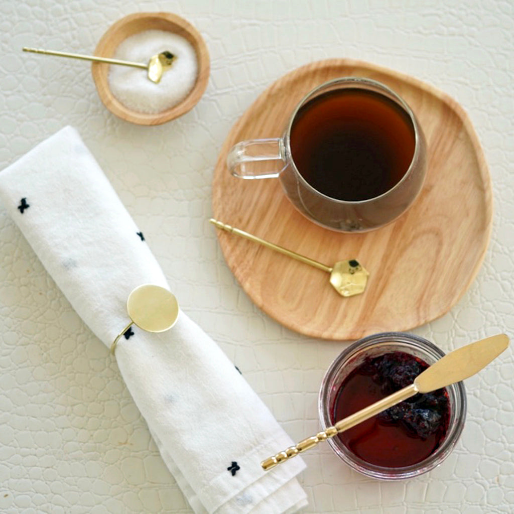 butter and jam knives are displayed in a table along with coffee and a spoon in a sugar recipient and a napkin with a napkin ring