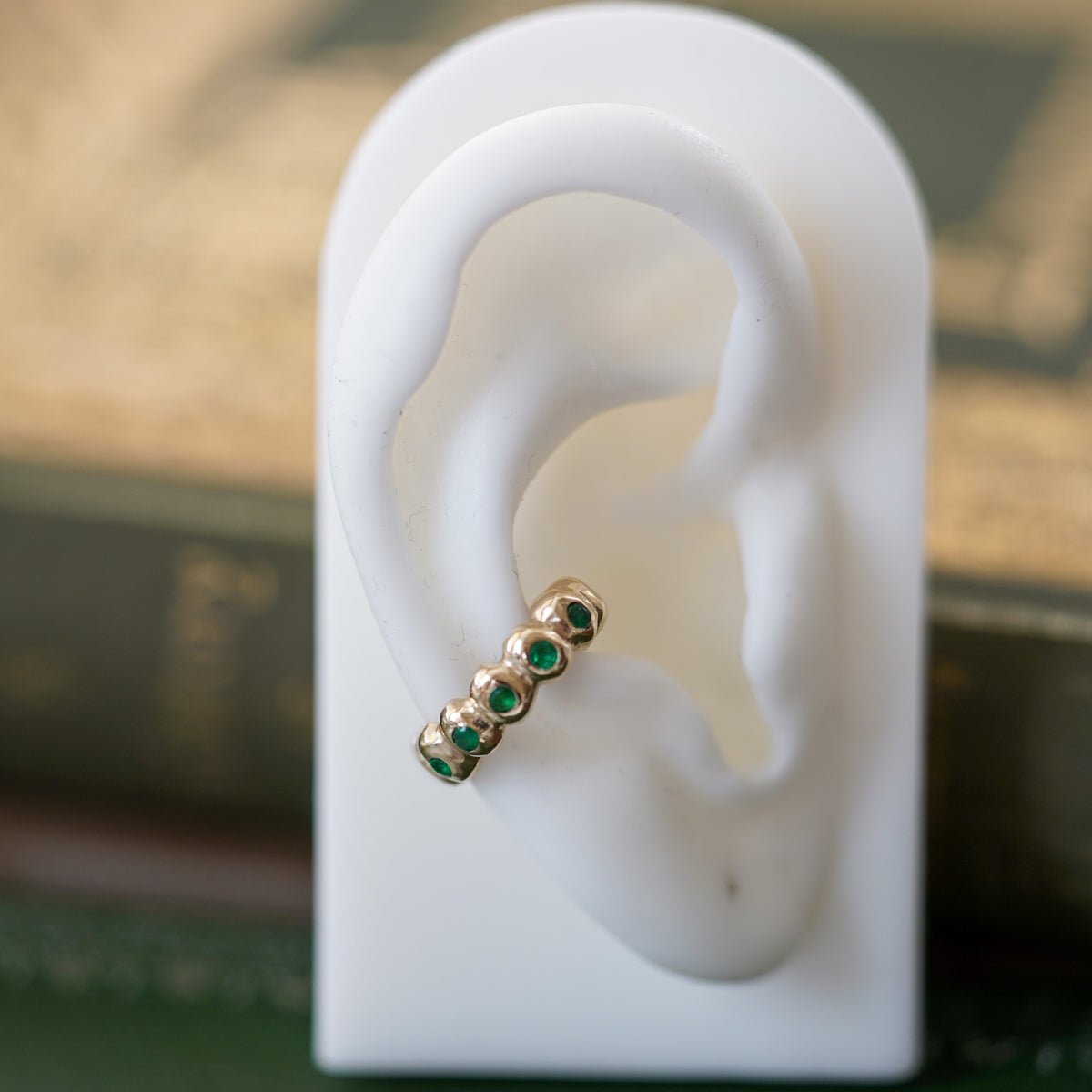 gold ear cuff with emeralds on a ear lobe