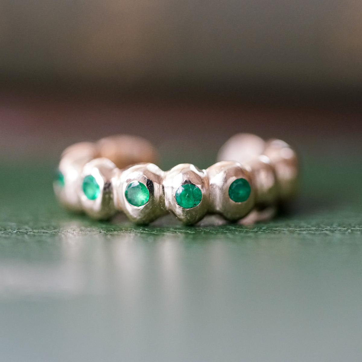 gold ear cuff with emeralds on a green surface 